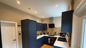 Une cuisine moderne avec des meubles bleu foncé, un plan de travail blanc et un mur de fond en briques apparentes.
