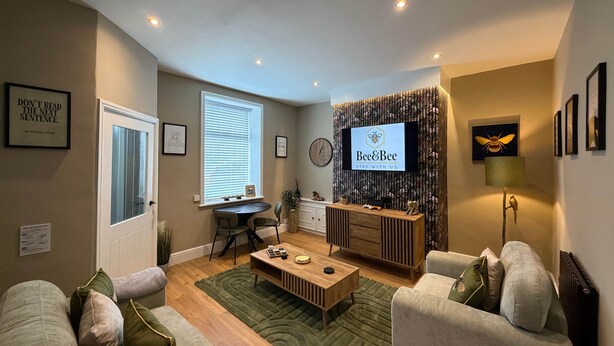 Un salon moderne avec un canapé, une table basse et un téléviseur fixé au mur, lequel est décoré d’un motif.