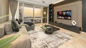 A modern living room with a large TV, comfortable seating, and a view of the city. - Grand JBR PentHouse Style (Dubai)