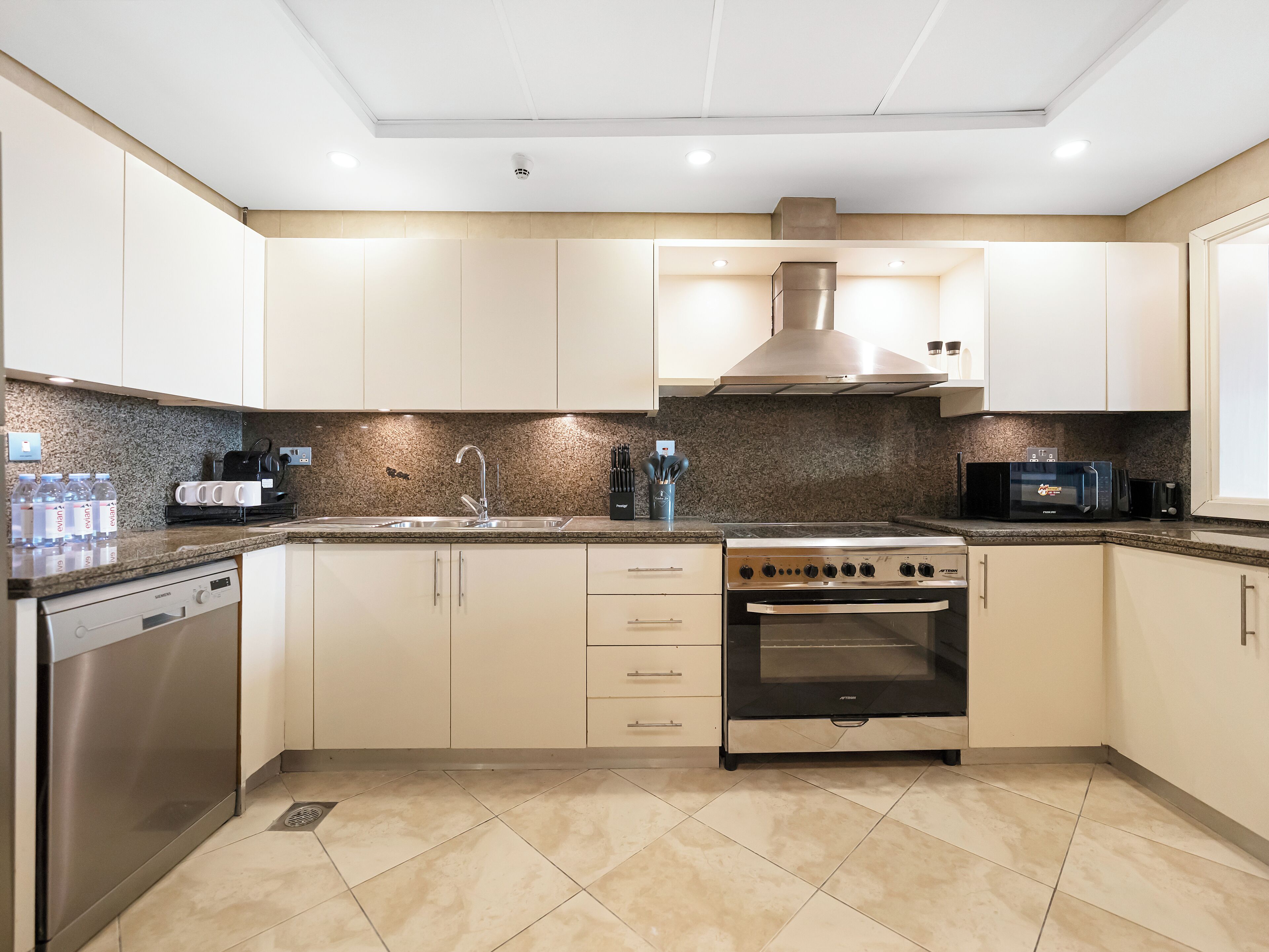 A modern kitchen with white cabinets, a stainless steel range hood, a built-in oven, and a granite countertop.