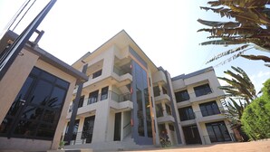 A multi-story building with balconies, large windows, and a paved ground area. - LUNARIS HOMES (Kigali)