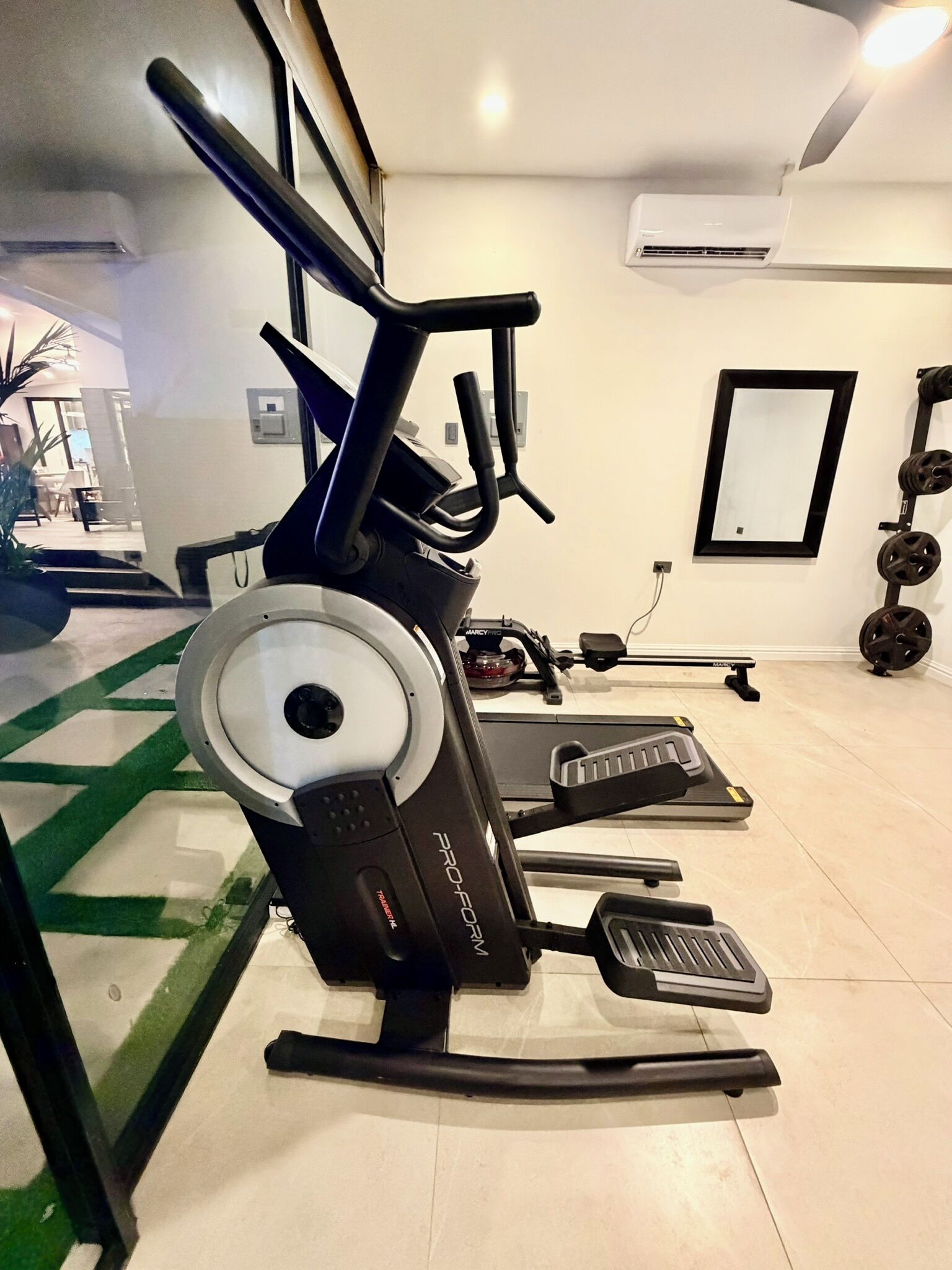 Une salle de sport équipée de machines de cardio, d’une zone pour la musculation et d’un grand miroir.
