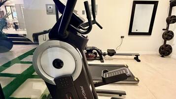 Une salle de sport équipée de machines de cardio, d’une zone pour la musculation et d’un grand miroir.
