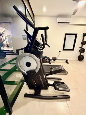 Une salle de sport équipée de machines de cardio, d’une zone pour la musculation et d’un grand miroir.