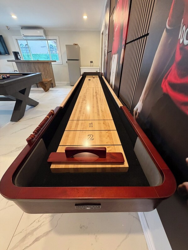 A shuffleboard table with numbered ends, a pool table, and a billiards table in a room with a large poster and a window. - Private 5 Bedroom Oasis in Prestigious Valsayn North - Prime Location (San Juan-Laventille Regional Corporation)