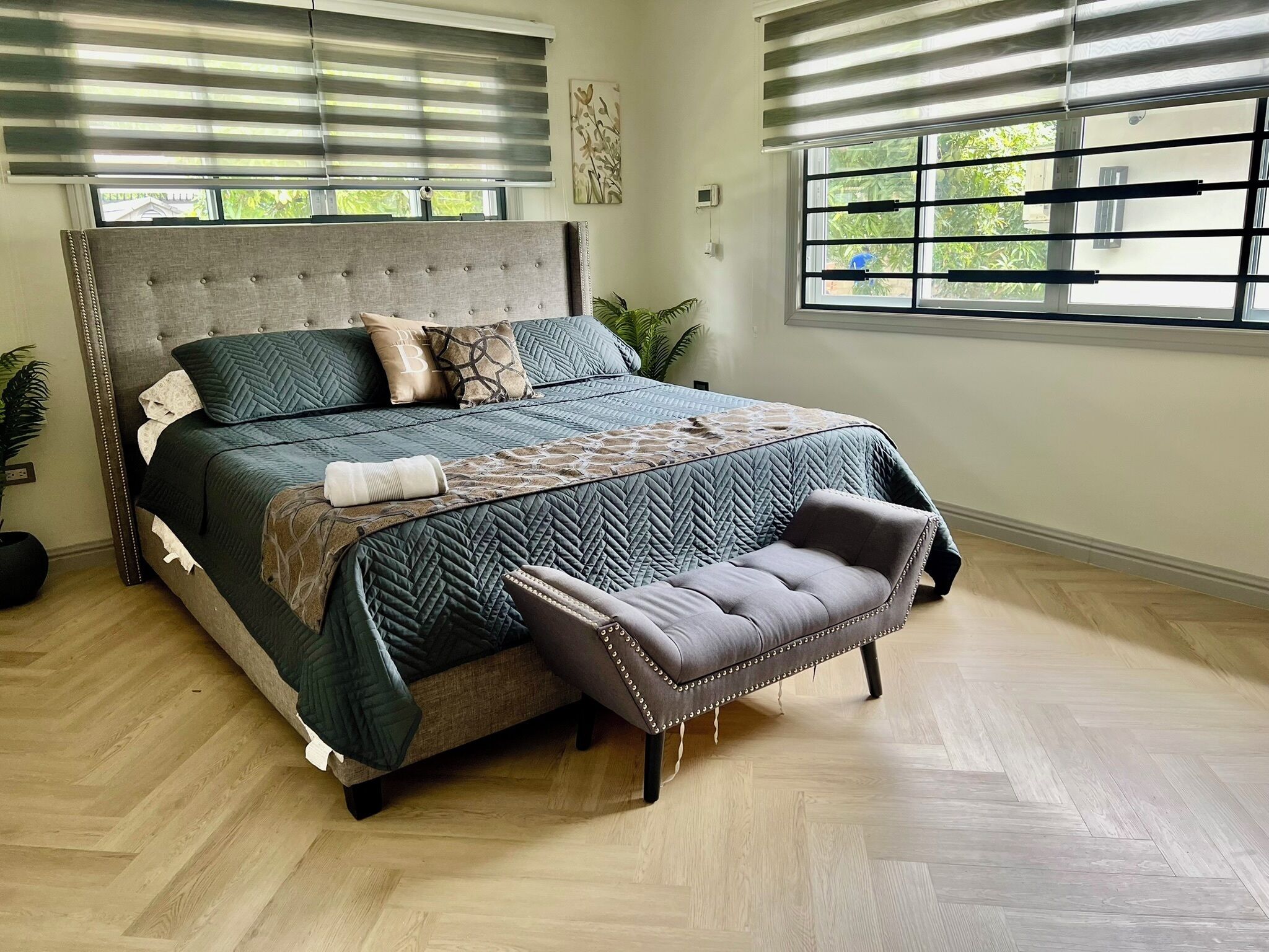 Une chambre à coucher avec un grand lit, un banc et une fenêtre équipée de stores.