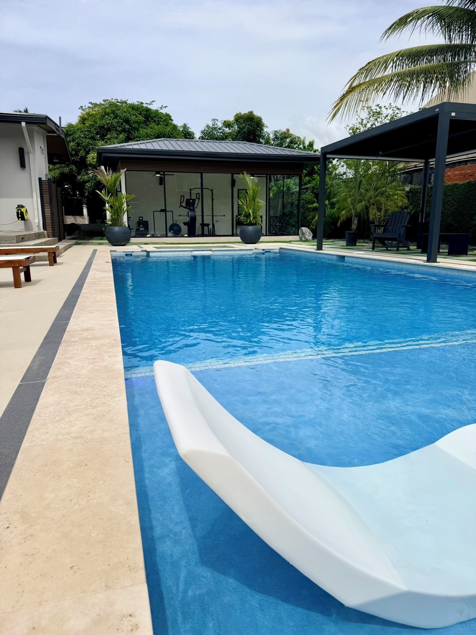 Une piscine avec un toboggan, entourée d’un patio aménagé avec des meubles d’extérieur et un espace salon couvert.