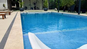 Une piscine avec un toboggan, entourée d’un patio aménagé avec des meubles d’extérieur et un espace salon couvert.