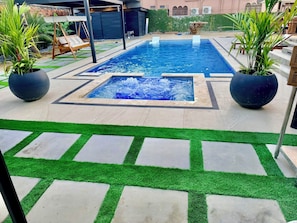 A rectangular swimming pool with a central water feature, surrounded by a patio with artificial grass and potted plants. - Private 5 Bedroom Oasis in Prestigious Valsayn North - Prime Location (San Juan-Laventille Regional Corporation)
