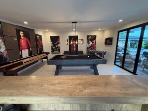 Une salle de billard équipée d’une table de billard, d’une table de baby-foot et ornée de souvenirs sportifs accrochés aux murs.