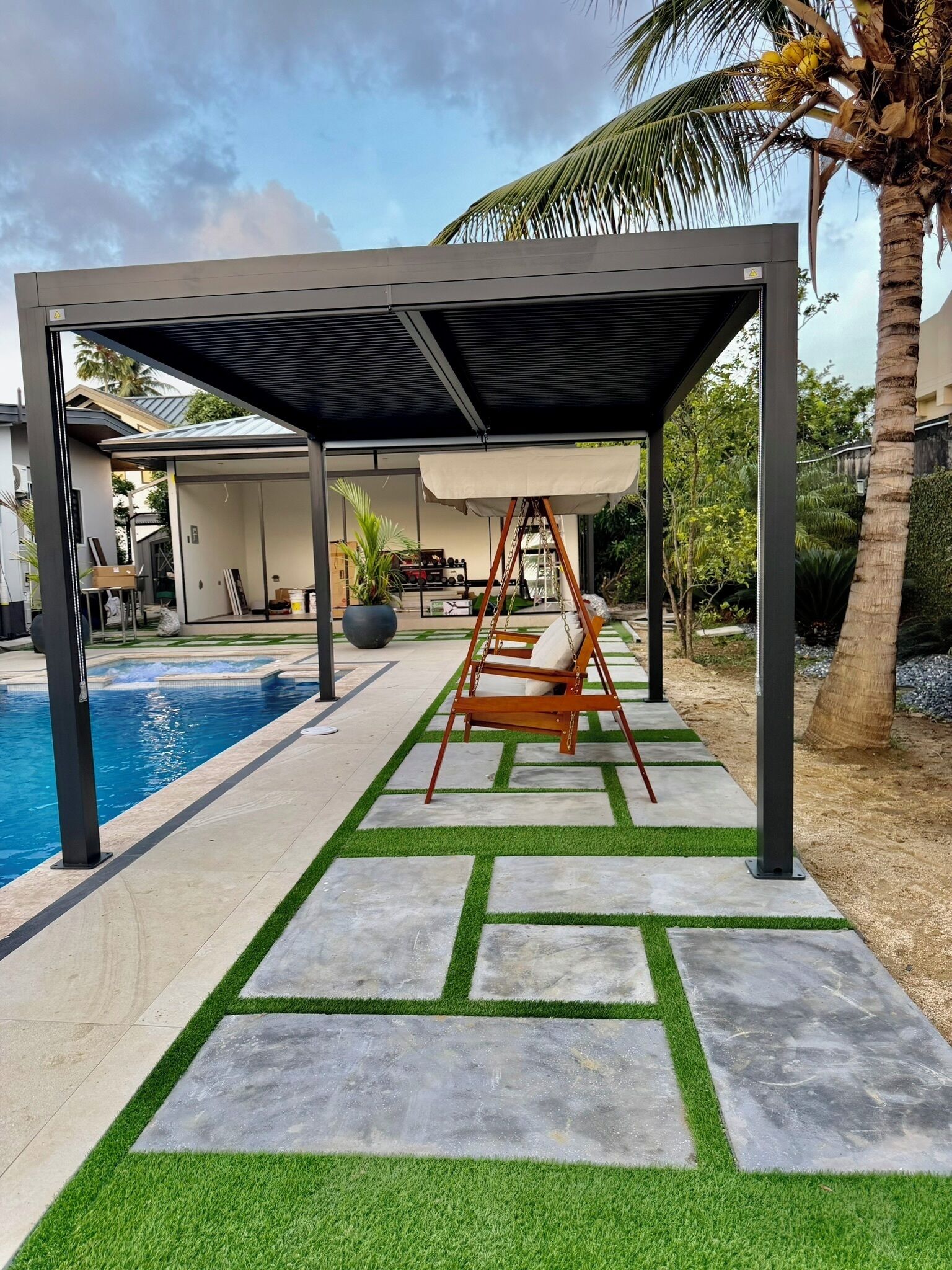 Un espace extérieur abrité, doté d’une balançoire, d’une piscine et d’une terrasse avec gazon synthétique et des carreaux en pierre.