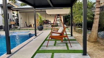 Un espace extérieur abrité, doté d’une balançoire, d’une piscine et d’une terrasse avec gazon synthétique et des carreaux en pierre.