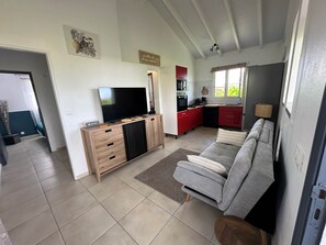 Sala de estar com sofá, televisão, móvel para home theater em madeira e área de cozinha com armários vermelhos e micro-ondas.