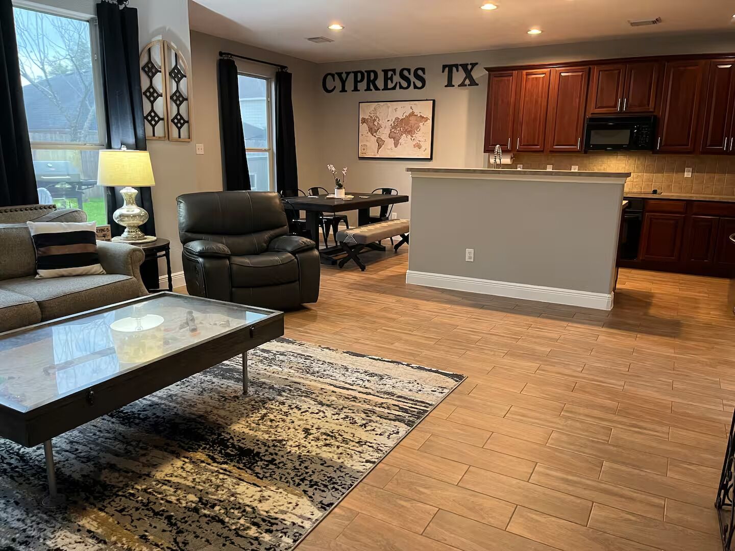 Una sala moderna con sofá, mesa de centro y alfombra. Hay un comedor con mesa y sillas, y una cocina con armarios de madera y microondas.