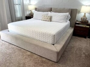 Una cama grande con colchón acolchado, cabecera con diseño de panal y dos mesitas de noche con lámparas.