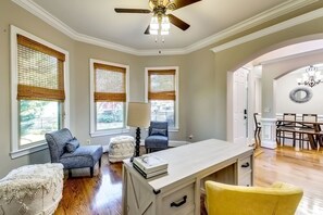Ein Zimmer mit Schreibtisch, zwei Stühlen, einer Lampe und einem Essbereich mit einem Chandelier.