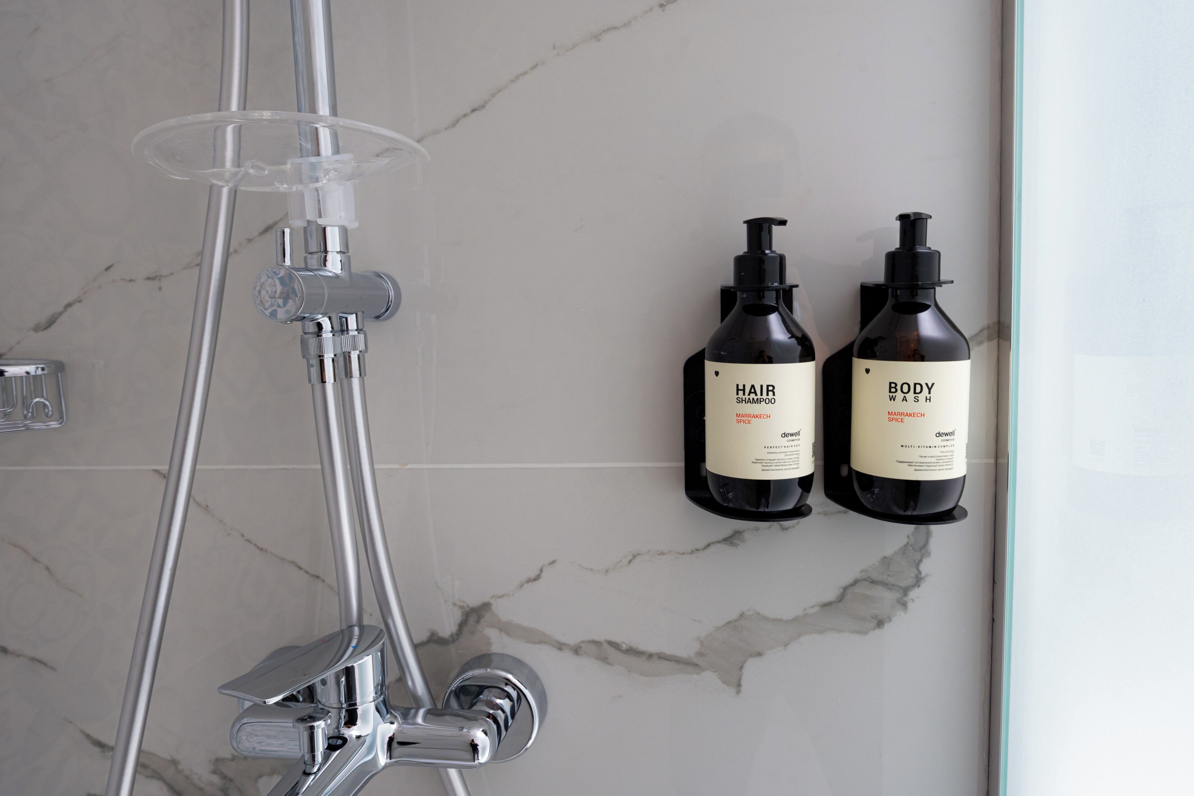 A bathroom with a modern shower setup and two bottles of hair and body wash on the wall.