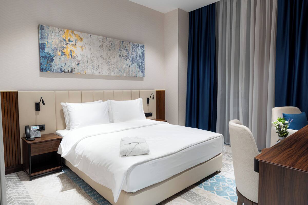 Habitación de hotel con una cama grande, una mesita de noche con teléfono, un escritorio con silla y un cuadro abstracto de gran tamaño en la pared.