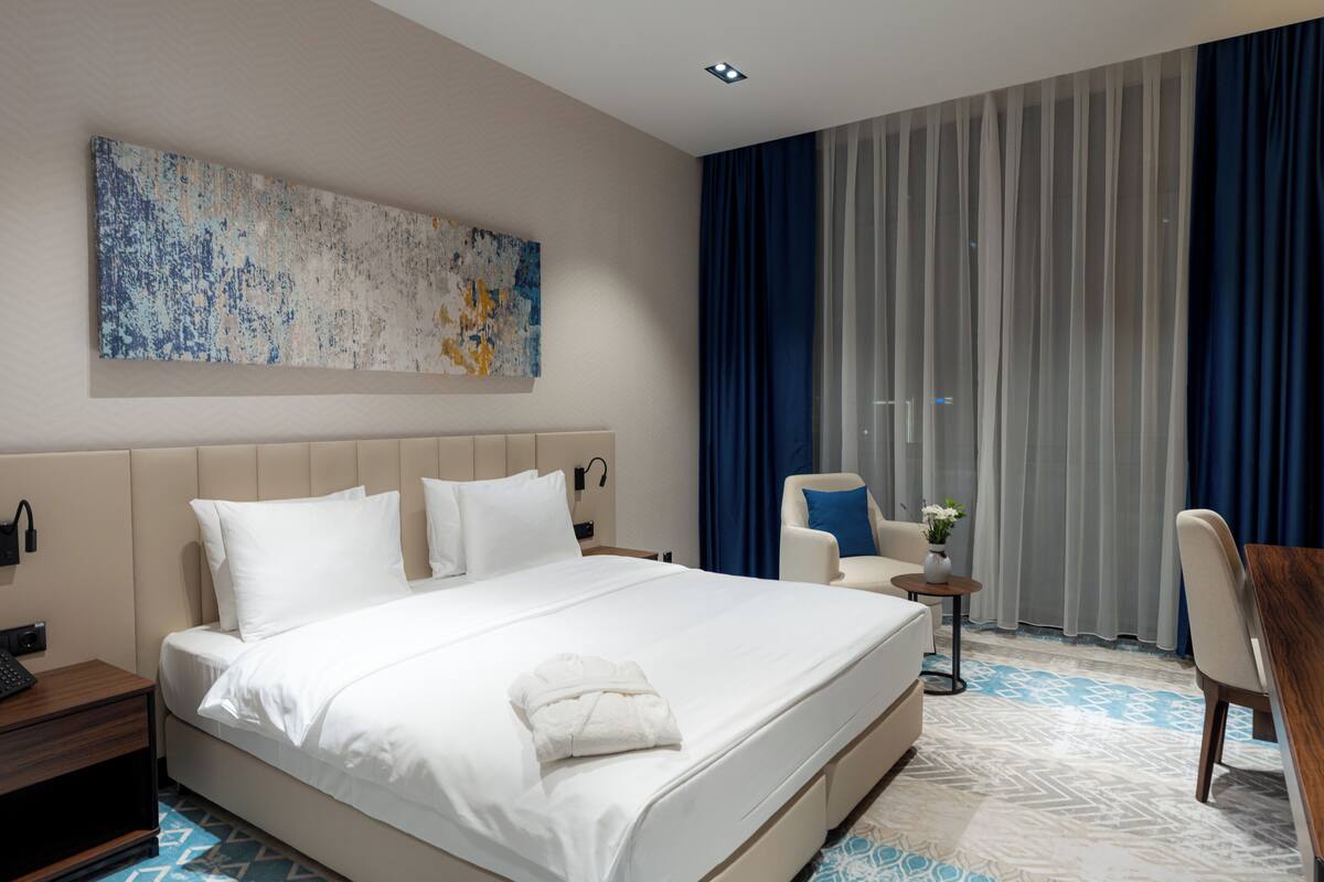 Una habitación de hotel moderna con una cama grande, un área de descanso y un ventanal con cortinas.