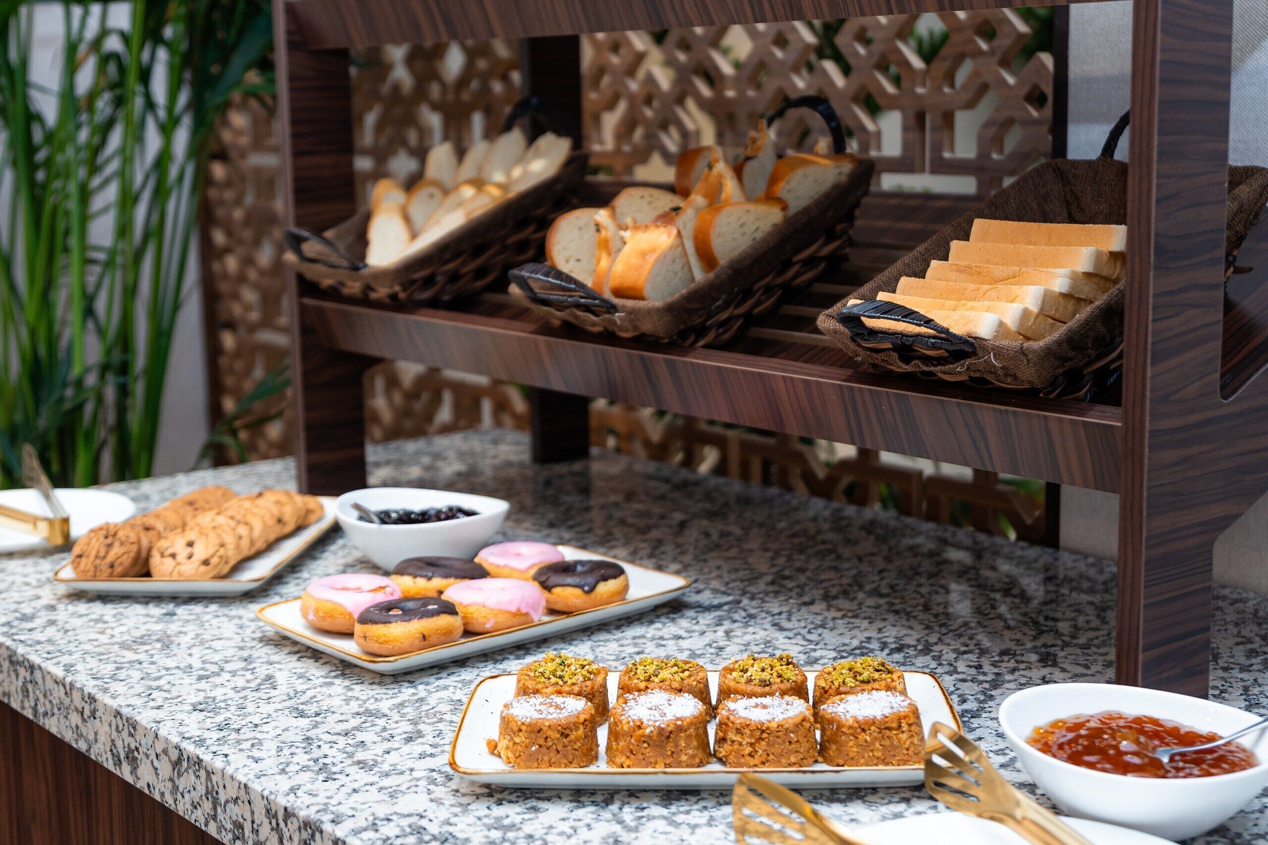 A buffet with various baked goods and pastries, including bread, cookies, and donuts.