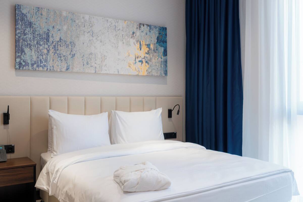 Habitación de hotel moderna con una cama grande, una mesita de noche, un teléfono en la pared y un cuadro abstracto de gran tamaño.