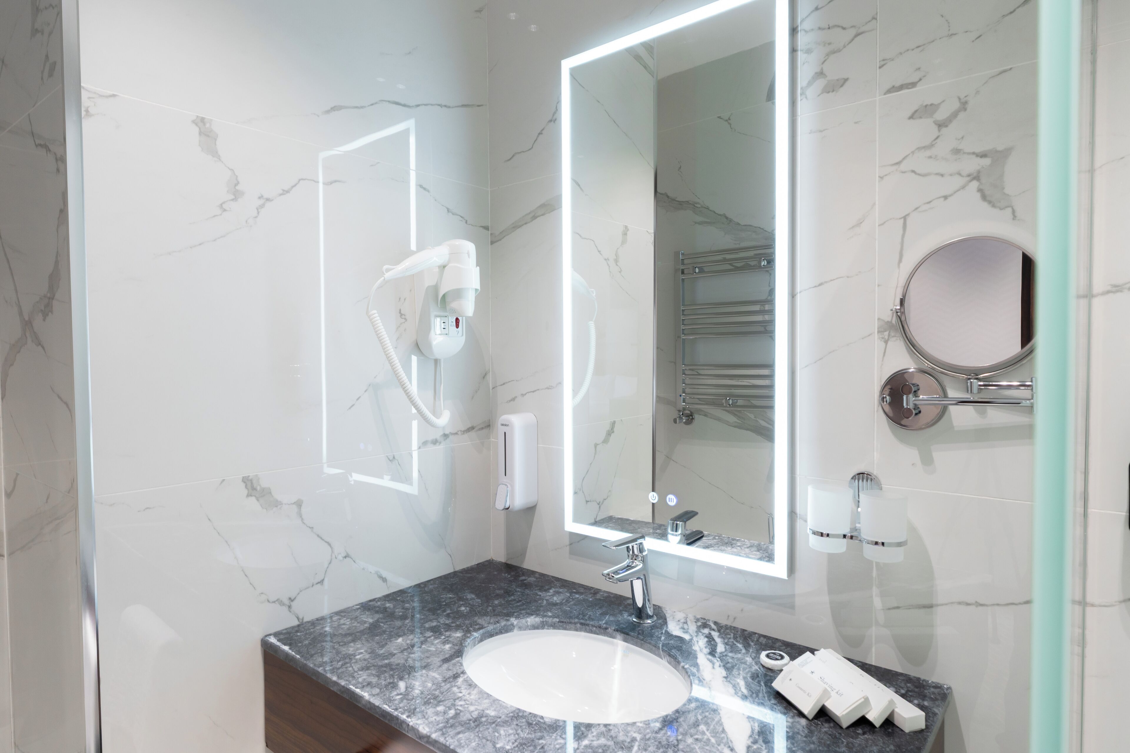 A modern bathroom with a marble wall, a sink with a faucet, a mirror, and a towel rack.