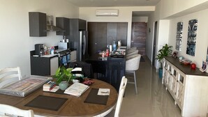 Een moderne keuken met donkere kastjes, een centraal kookeiland en een eethoek met een ronde tafel en stoelen.