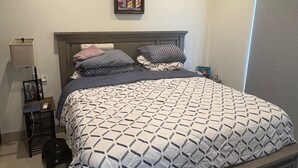 Een slaapkamer met een bed, een plafondventilator, een nachtkastje, een lamp en een ingelijst beeld aan de muur.