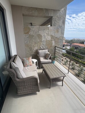 A balcony with wicker furniture, a stone wall, and a view of the city. - 2-bedroom condo in tranquil Cabo San Lucas with AC and gym and full Ocean View (Cabo San Lucas)