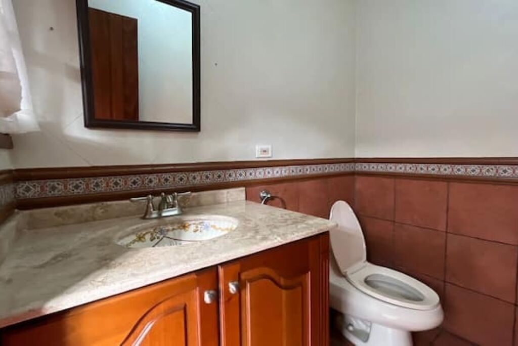 A bathroom with a marble sink, wooden cabinets, a white toilet, and a decorative tile border.