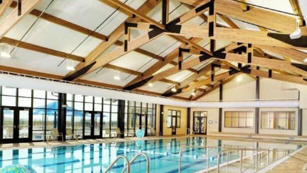 An indoor swimming pool with clear glass walls, wooden beams, and lounge chairs. - Galena Getaway (Galena)