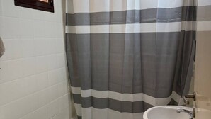 A bathroom with a striped shower curtain, a white sink, and a toilet. - Apartment in the heart of downtown Mendoza. (Mendoza)