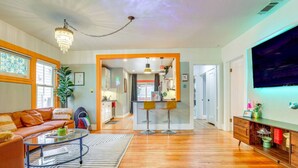 A living room with a sofa, coffee table, and TV. There is a kitchen in the background. - Midtown Oasis | BBQ, Deck, Games & Artistic Vibes (Sacramento)