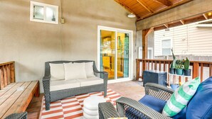 A covered patio with wicker furniture, a checkered rug, and a wooden deck. - Midtown Oasis | BBQ, Deck, Games & Artistic Vibes (Sacramento)