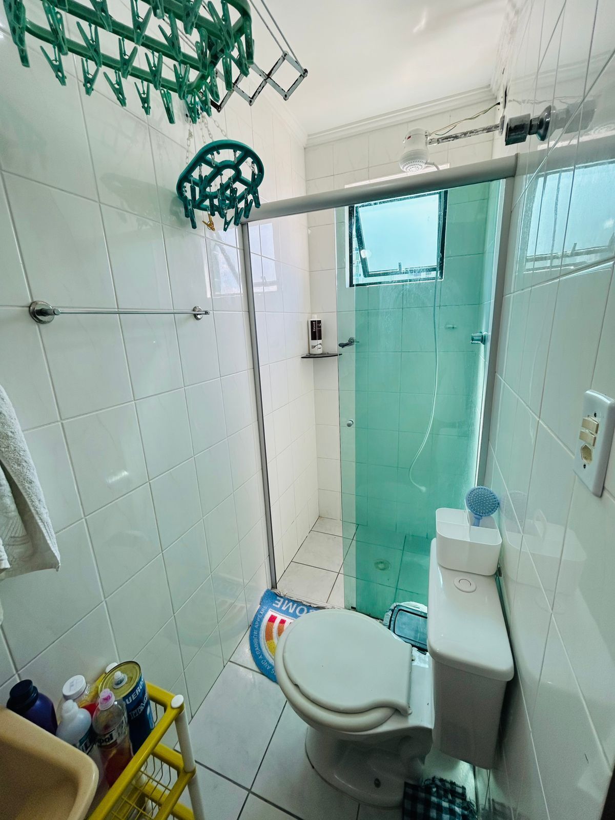 A bathroom with a toilet, a shower stall with a glass door, a towel rack, and a small shelf with toiletries.