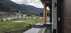 A modern building with a stone exterior, a paved driveway, and a view of a mountainous landscape. - Whistler Mountain Mist Retreat with hottub/pooltable (whistler)