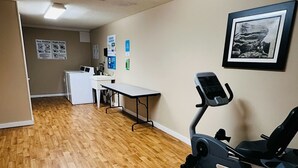 A laundry room with a washing machine, dryer, and ironing board. There is a desk with a chair and a framed picture on the wall. - Extended Stay- Full Kitchen 1BR apartment in Downtown Pittsfield (Pittsfield)