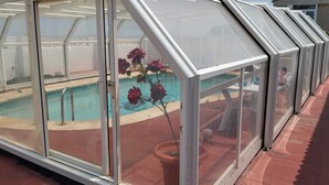 A covered outdoor area with a pool, enclosed by a glass structure with a peaked roof.