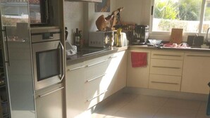 A kitchen with a microwave, oven, and various appliances on the counter. There is a window with a view of greenery outside.