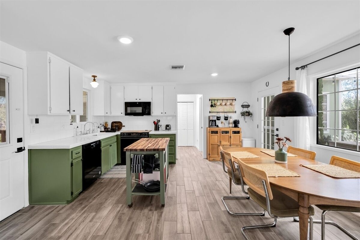 Une cuisine moderne avec des meubles blancs, un îlot central en bois et un coin repas comprenant une grande table et des chaises.