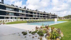 Un edificio moderno de varios pisos con piscina, mobiliario exterior y jardines ajardinados.