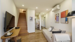 Een moderne woonkamer met een houten trap, een flatscreen-tv, een bank en een eethoek.
