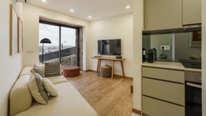 Een moderne woonkamer met een bank, een televisie, een keukenhoek en een groot raam.