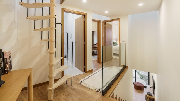 Een modern interieur met een houten spiraaltrap, een glazen balustrade en uitzicht op een eethoek.