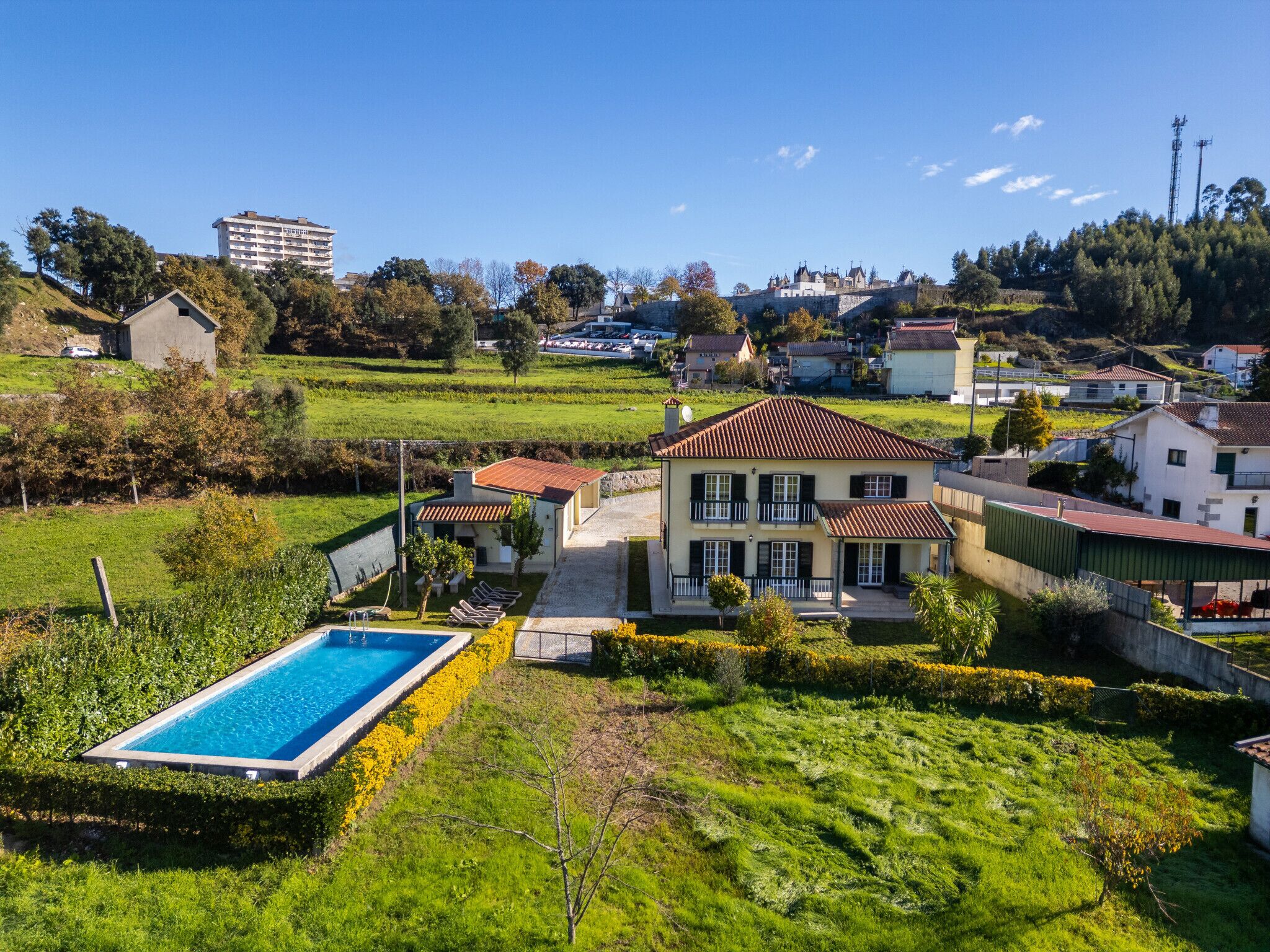 Una casa grande de dos pisos con piscina, rodeada de abundante vegetación y un paisaje montañoso.
