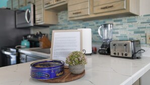 Een keuken met houten kastjes, een blender, een broodrooster en een blik Royal Dansk op het aanrecht.