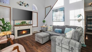 Een moderne woonkamer met een open haard, een grijze bank en een flatscreen televisie.