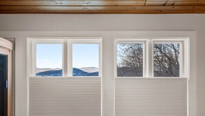 Ein Zimmer mit zwei Fenstern, jedes mit Blick auf Berge und Bäume.