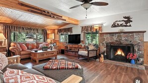A cozy living room with a stone fireplace, wooden furniture, a television, and a ceiling fan. - Cozy cabin right at Lewis Creek Trail, near  Yosemite, Bass lake (Oakhurst)