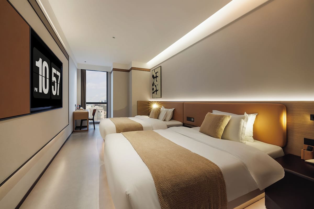 Une chambre d’hôtel moderne avec deux lits, un bureau et une grande fenêtre.